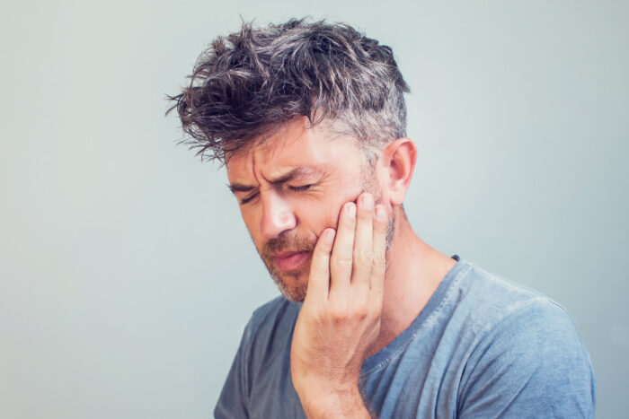 Middle-aged man with sensitive teeth cringes in pain and touches his cheek