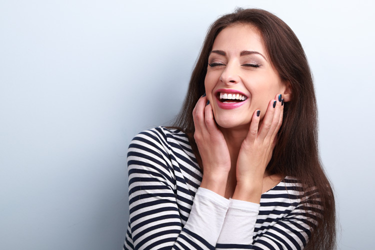 Brunette woman smiles with her dream smile after a full-mouth restoration while wearing a striped shirt