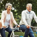 A husband and wife with snap-on dentures and dental implants smile as they ride bikes together