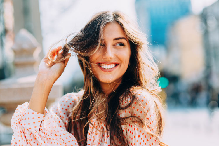 Brunette woman with sensitive teeth smiles because she safely whitened her teeth at Optima Dental Spa