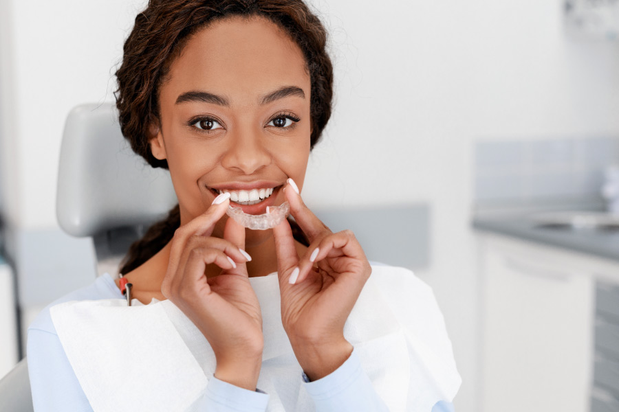 Brunette woman smiles as she puts in her ClearCorrect aligners to straighten her teeth