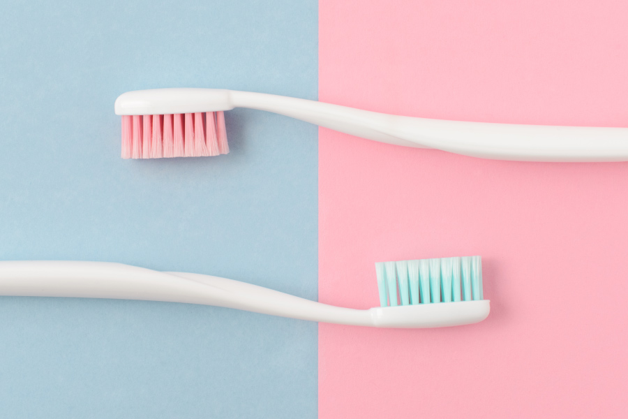 A white toothbrush with blue bristles and a white toothbrush with pink bristles against a blue and purple background